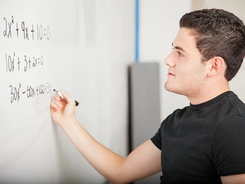Ein junger Mann rechnet eine Matheaufgabe an der Tafel.