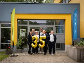 Sechs Personen stehen vor dem Eingang des CJD in Ilmenau. Sie halten große, goldene Folienballons 35.