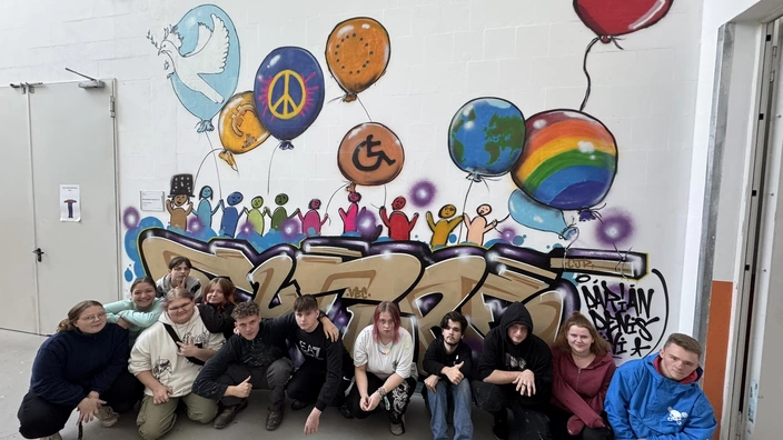 Eine Gruppe von Jugendlichen vor einem großen, bunten Graffiti