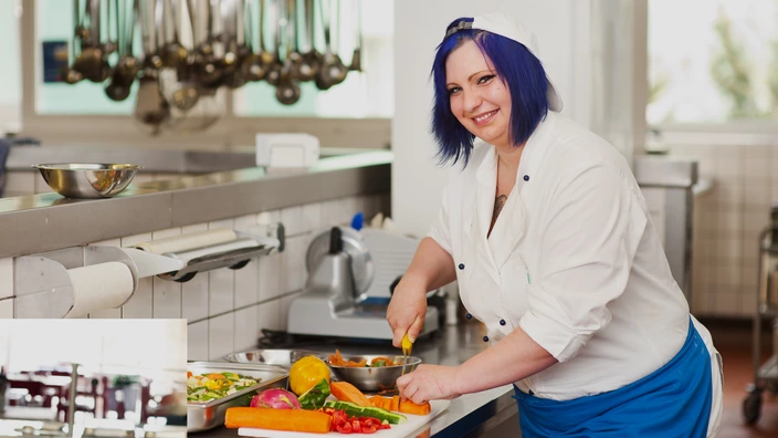 Eine Auszubildende schneidet Gemüse in der Küche.