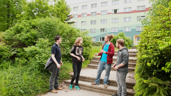 Vier Jugendliche stehen auf einer Treppe und unterhalten sich. Im Hintergrund ist das CJD Jugendgästehaus/Internat zu sehen.