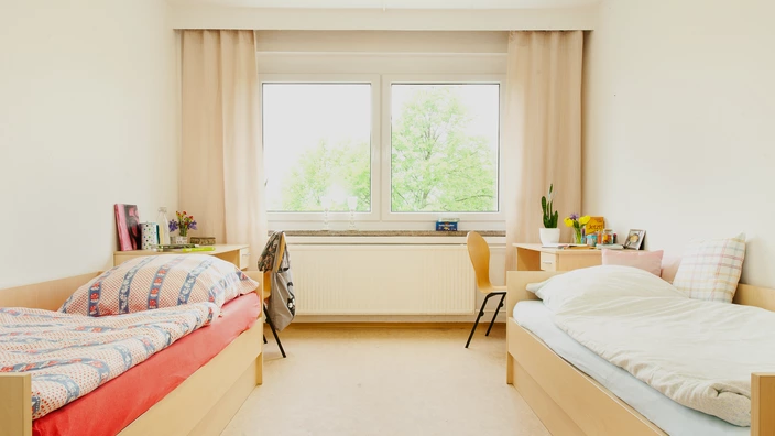 Einblick in ein Doppelzimmer im CJD Jugendgästehaus/Internat Ilmenau. Zu sehen sind zwei Betten und zwei Schreibtische.