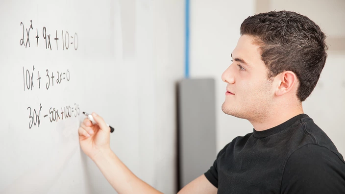 Ein junger Mann rechnet eine Matheaufgabe an der Tafel.