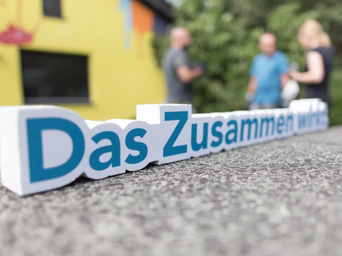 Schriftzug „Das Zusammen wirkt.“ im Vordergrund, im Hintergrund unscharfe Personen, Gemeinschaft und Zusammenhalt beim CJD.